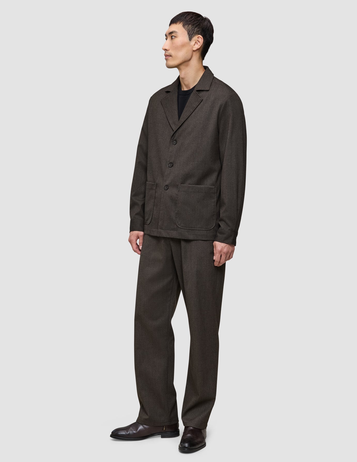 En mand iført en Atelier Overshirt i mørkebrun i et elegant dansk design med matchende bukser.
